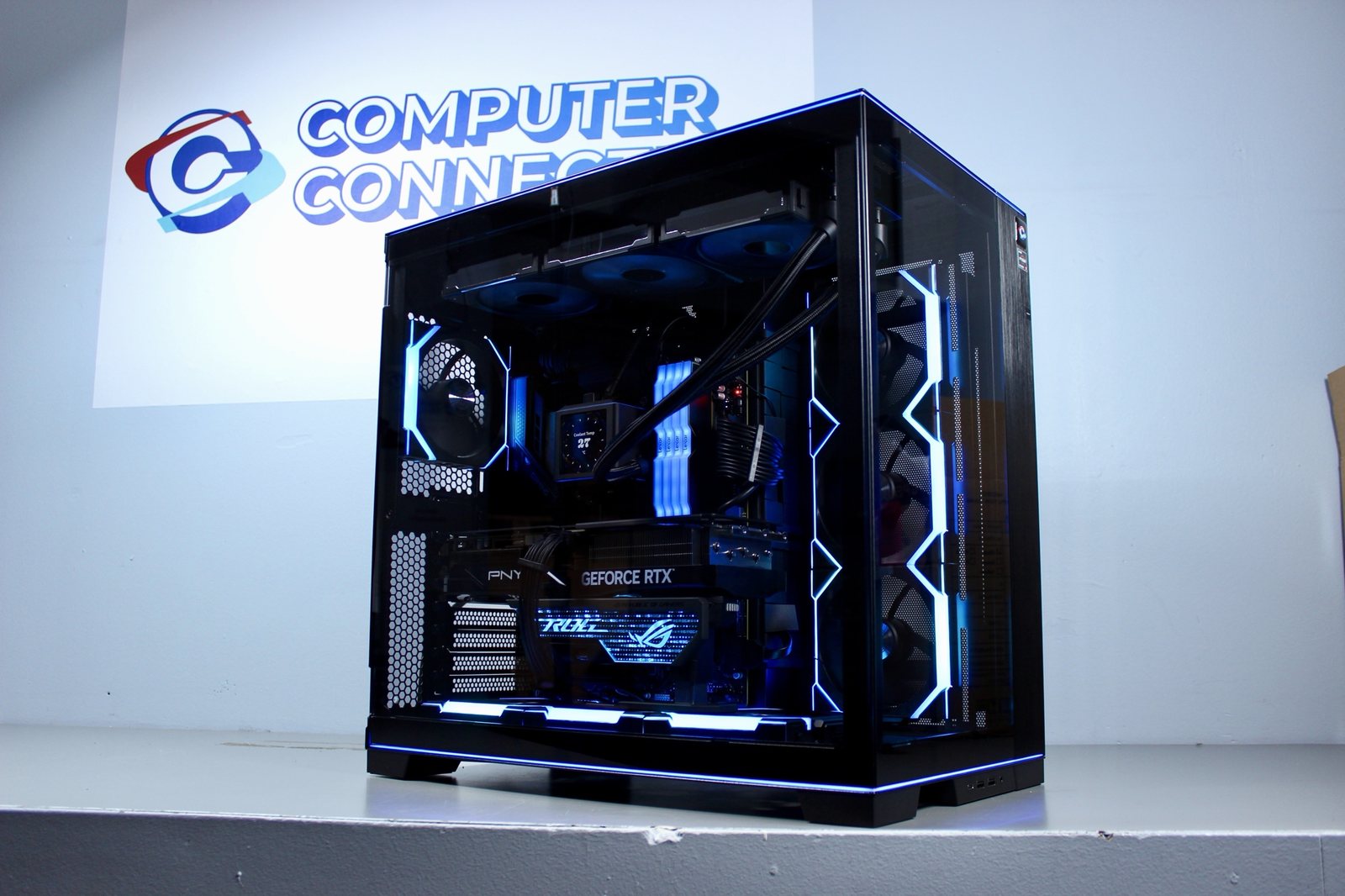 Black Lian Li custom PC with a PNY GeForce RTX card and blue lighting, in front of the Computer Connection logo wall