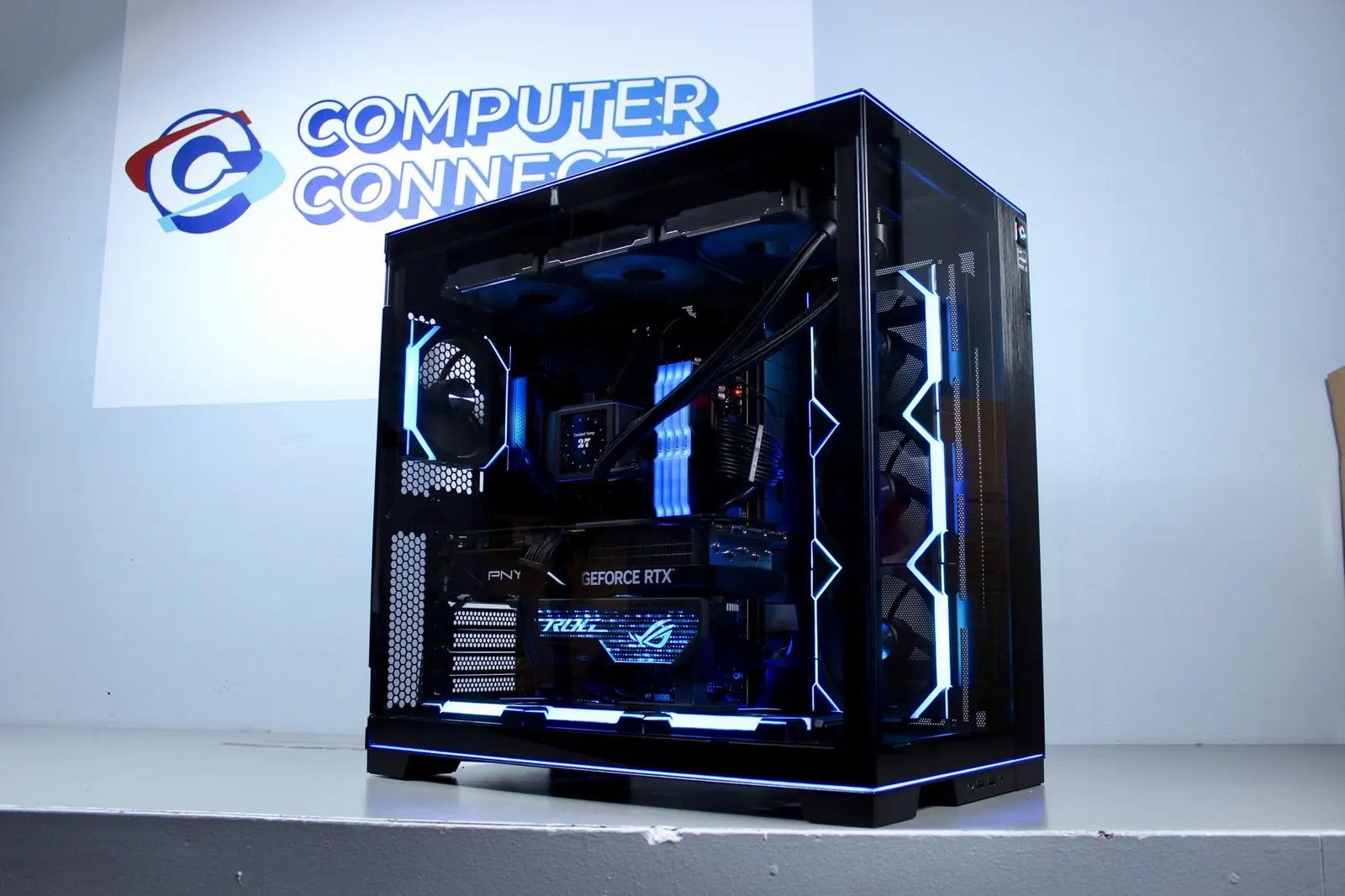 Black Lian Li custom PC with a PNY GeForce RTX card and blue lighting, in front of the Computer Connection logo wall